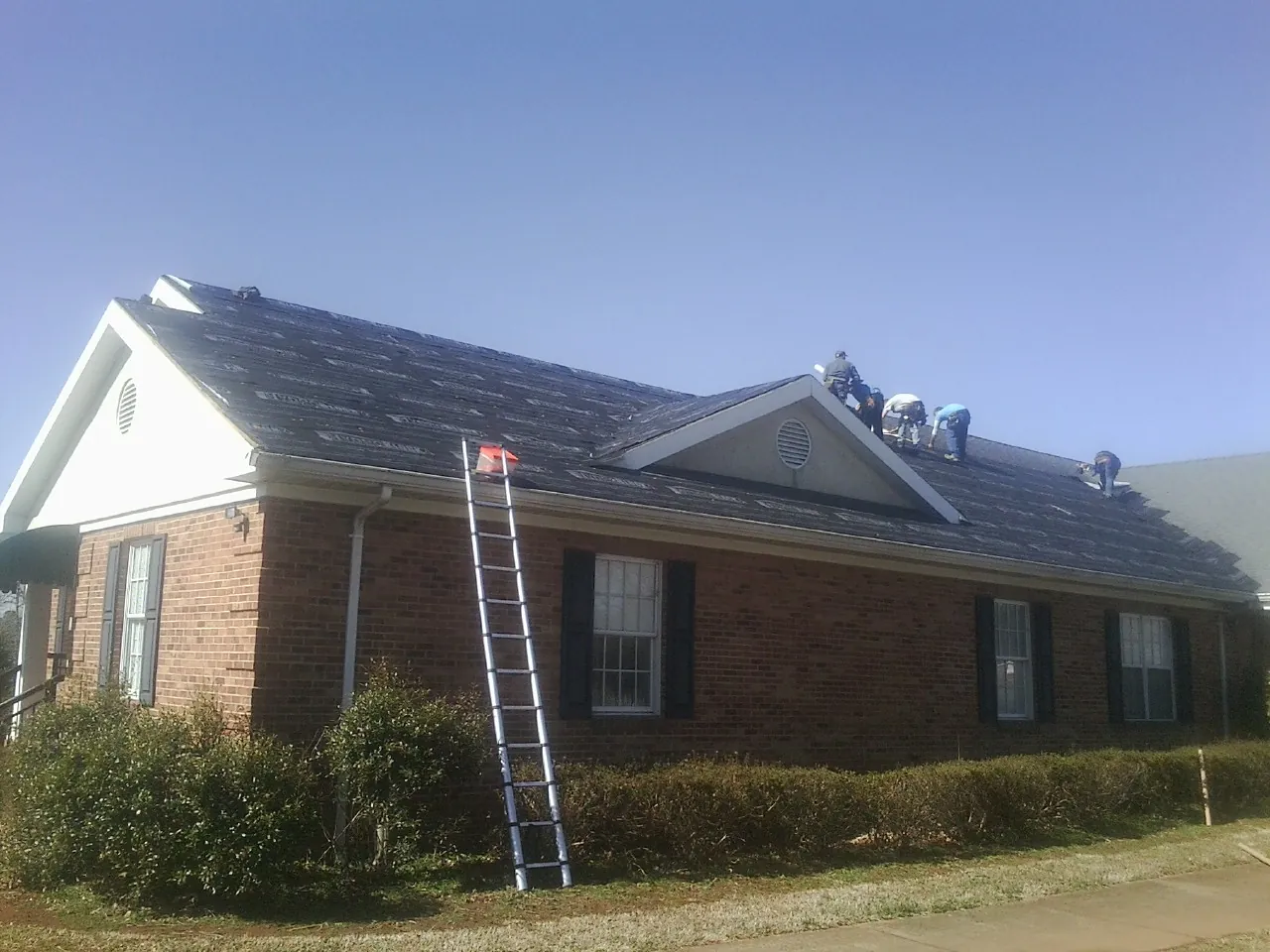 Crew tearing shingles off a brick ranch roof with a ladder set — Metal Roof Repair work by our crew in Summer Shade