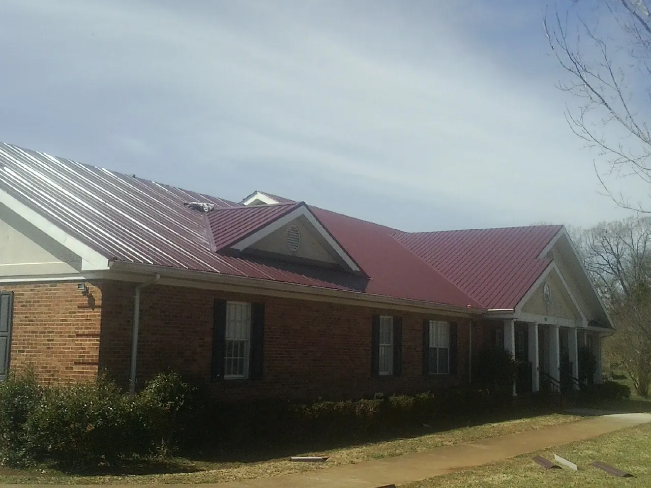 Red metal roof with gabled entries on a long brick building, from a Hail Damage Roof Repair job in Summer Shade