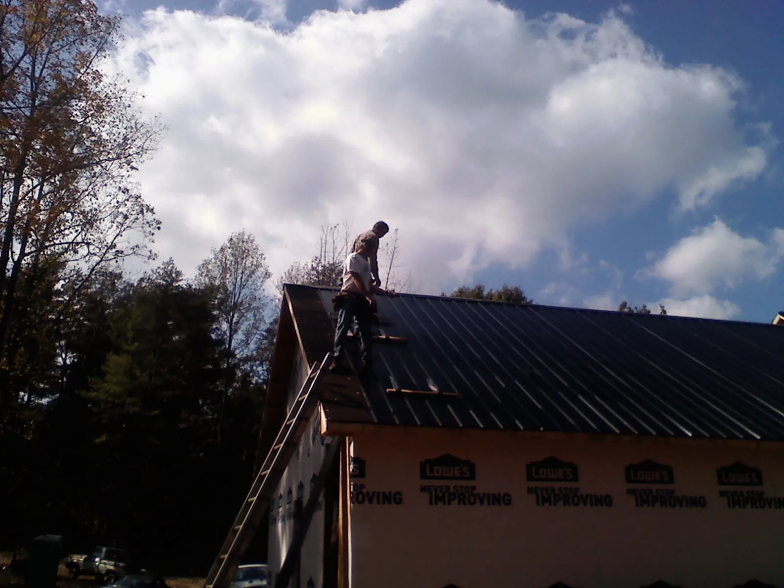Roofer fastening dark metal panels high against a cloudy sky, from a Roof Inspection job in Summer Shade