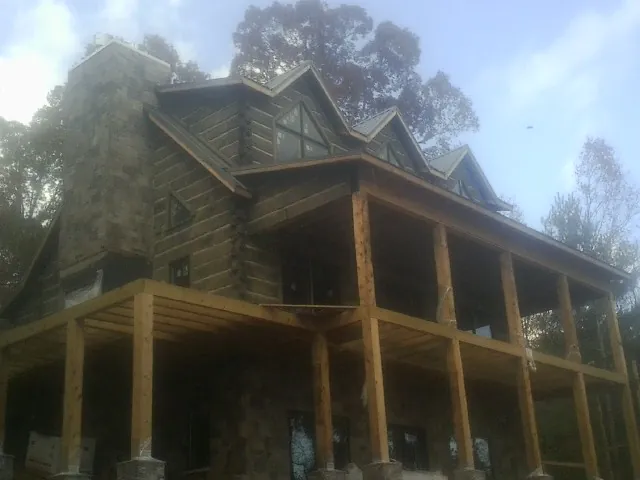 Stone chimney and dormers on a large log home with a timber porch in Summer Shade