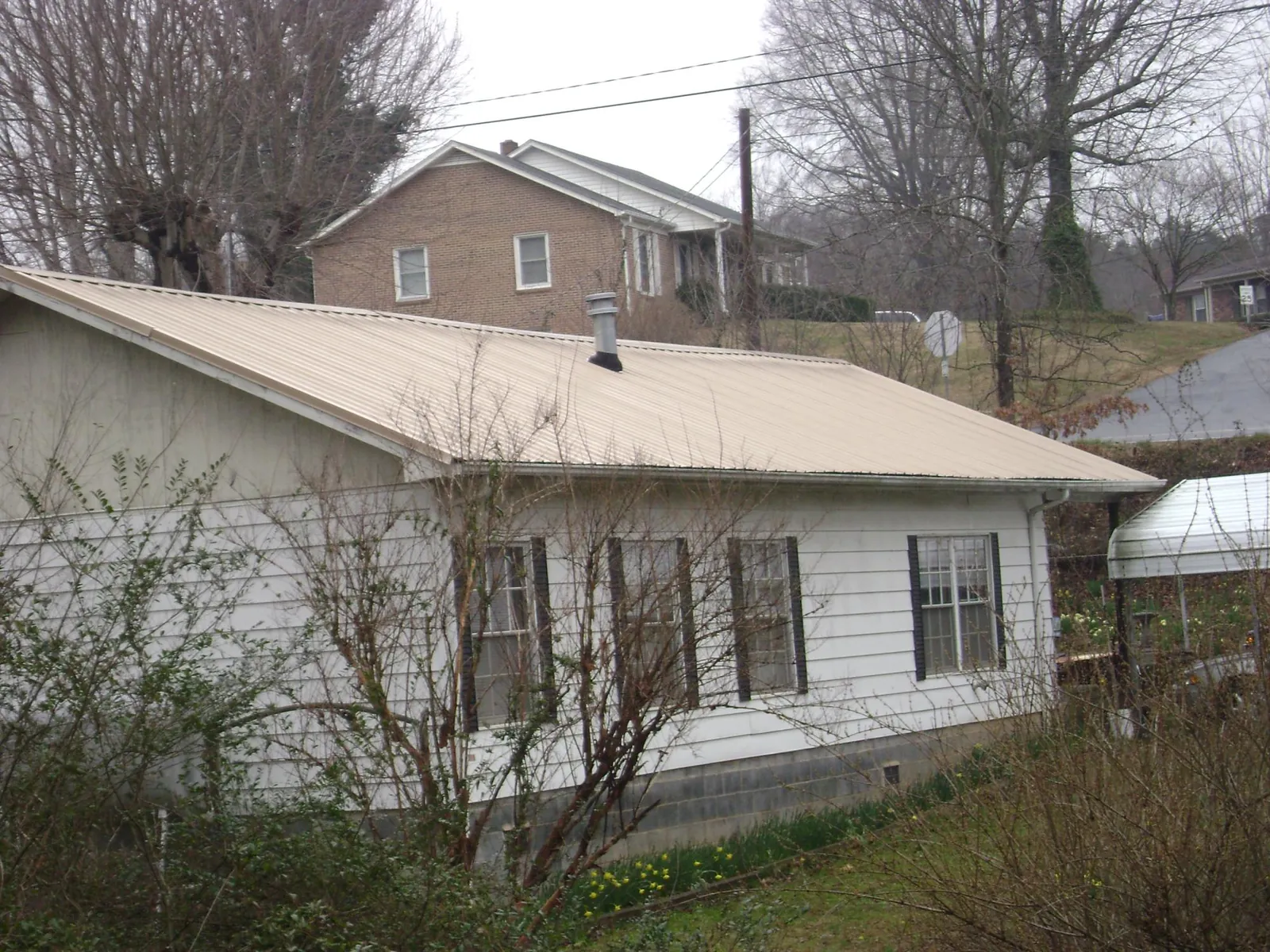 Tan metal roof on a white sided house set into a hillside — Commercial Roofing by Roofing Brothers in Summer Shade